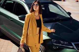 bellissimo luce del sole. giovane alla moda donna nel Borgogna colorato cappotto a giorno con sua auto foto