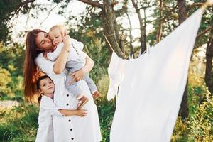 casalinga essiccazione Abiti. giovane madre con sua poco figlia e figlio è all'aperto nel il foresta. bellissimo luce del sole foto