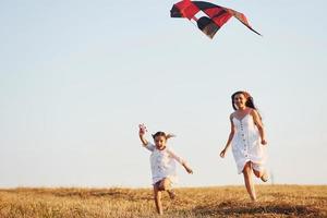 contento madre con sua poco figlia avere divertimento di giocando con aquilone all'aperto su il campo foto