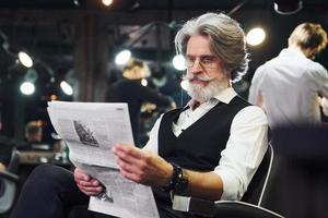 lettura giornale. elegante moderno anziano uomo con grigio capelli e barba è in casa foto