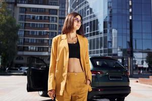 moderno attività commerciale edificio a sfondo. giovane alla moda donna nel Borgogna colorato cappotto a giorno con sua auto foto