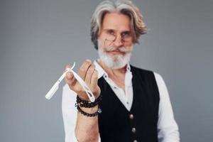 barbiere Strumenti. contro grigio sfondo. elegante moderno anziano uomo con grigio capelli e barba è in casa foto