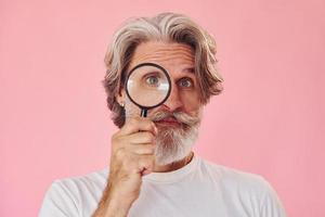 utilizzando ingrandimento bicchiere. elegante moderno anziano uomo con grigio capelli e barba è in casa foto