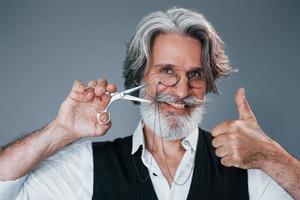 barbiere Strumenti. contro grigio sfondo. elegante moderno anziano uomo con grigio capelli e barba è in casa foto