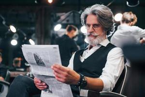 lettura giornale. elegante moderno anziano uomo con grigio capelli e barba è in casa foto