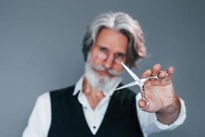 barbiere Strumenti. contro grigio sfondo. elegante moderno anziano uomo con grigio capelli e barba è in casa foto