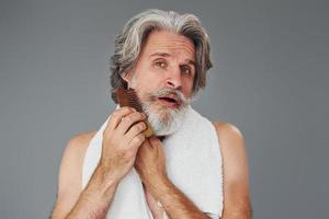 assunzione cura di viso e pelle chiarezza. elegante moderno anziano uomo con grigio capelli e barba è in casa foto