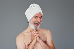 con bianca asciugamano su testa. elegante moderno anziano uomo con grigio capelli e barba è in casa foto