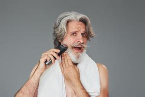 assunzione cura di barba. elegante moderno anziano uomo con grigio capelli è in casa foto