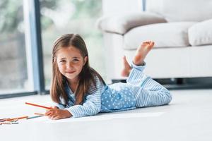 dire bugie su il pavimento e disegno. carino poco ragazza in casa a casa solo foto