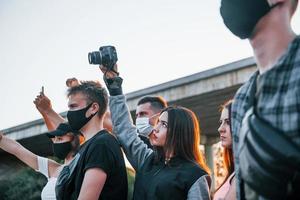 fotografo con telecamera. gruppo di protestare giovane persone quello in piedi insieme. attivista per umano diritti o contro governo foto