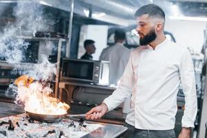 frittura padella è su fuoco. capocuoco nel bianca uniforme cucinando cibo a cucina. occupato giorno a opera foto