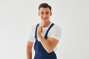 Spettacoli bicipite. pronto per opera. maschio lavoratore nel blu uniforme in piedi dentro di studio contro bianca sfondo foto