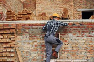 si arrampica su. costruzione lavoratore nel uniforme e sicurezza attrezzatura avere lavoro su edificio foto