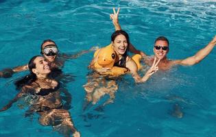 utilizzando giallo colorato anatra per nuotare. gruppo di giovane contento persone avere divertimento nel nuoto piscina a giorno foto