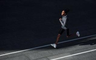 veloce corridore. giovane africano americano donna nel allegro Abiti avere allenarsi all'aperto a giorno foto