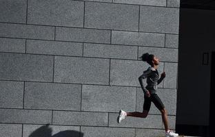 attivo corridore. giovane africano americano donna nel allegro Abiti avere allenarsi all'aperto a giorno foto