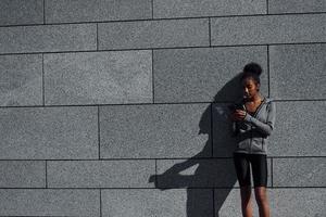 usi Telefono. giovane africano americano donna nel allegro Abiti avere allenarsi all'aperto a giorno foto