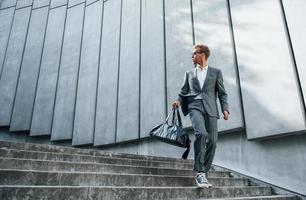 andando giù di il scale. giovane uomo d'affari nel grigio formale indossare è all'aperto nel il città foto
