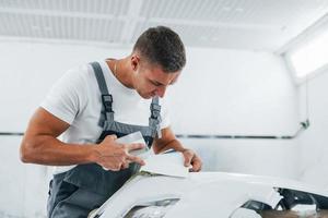 dettagliato opera. caucasico automobile riparatore nel uniforme avere lavoro nel box auto foto