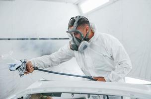 nel protettivo maschera. pittura il macchina. caucasico automobile riparatore nel uniforme lavori nel box auto foto