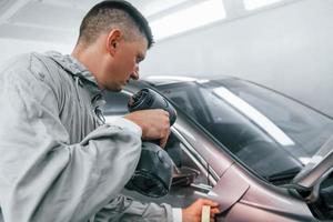 l'applicazione nuovo colore. caucasico automobile riparatore nel uniforme lavori nel box auto foto