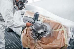 pittura lavoro nel progresso. caucasico automobile riparatore nel uniforme lavori nel box auto foto