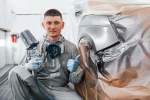 si siede vicino appena dipinto macchina. caucasico automobile riparatore nel uniforme lavori nel box auto foto