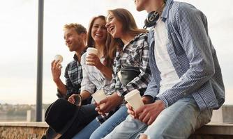 soleggiato tempo atmosferico. potabile caffè. gruppo di giovane allegro amici quello è all'aperto avendo divertimento insieme foto