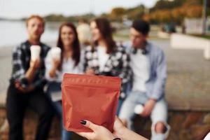 rosso pacchetto di caffè. gruppo di giovane allegro amici quello è all'aperto avendo divertimento insieme foto