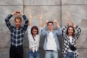 fabbricazione diverso gesti. gruppo di giovane positivo amici nel casuale Abiti in piedi insieme contro grigio parete foto