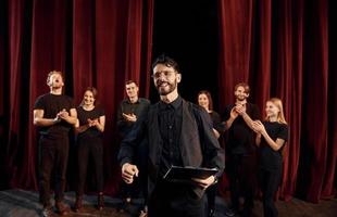 uomo è praticante il suo ruolo. gruppo di attori nel buio colorato Abiti su prova nel il Teatro foto