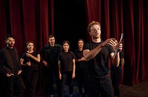 uomo con bloc notes pratica il suo ruolo. gruppo di attori nel buio colorato Abiti su prova nel il Teatro foto