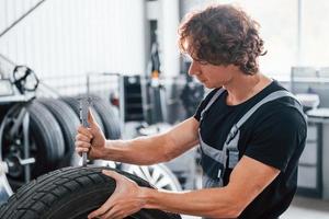 lavori con pneumatico. adulto uomo nel grigio colorato uniforme è nel il automobile salone foto