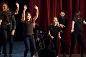 contento persone festeggiare successo. gruppo di attori nel buio colorato Abiti su prova nel il Teatro foto