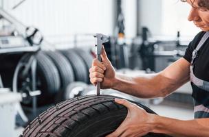 lavori con pneumatico. adulto uomo nel grigio colorato uniforme è nel il automobile salone foto