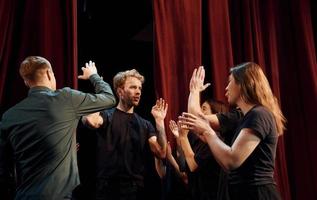 dando alto cinque, festeggiare successo. gruppo di attori nel buio colorato Abiti su prova nel il Teatro foto