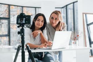 telecamera su tripode è registrazione. Due giovane femmina liberi professionisti Lavorando in casa nel il ufficio con il computer portatile foto