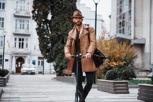 su il elettrico scooter. giovane maschio modello nel alla moda Abiti è all'aperto nel il città a giorno foto