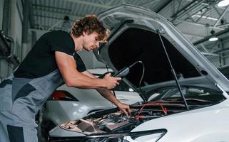 test macchine elettronica. adulto uomo nel grigio colorato uniforme lavori nel il automobile salone foto