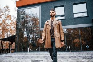 in piedi contro edificio con bicchiere porte. giovane maschio modello nel alla moda Abiti è all'aperto nel il città a giorno foto