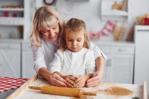 impasta il Impasto. anziano nonna con sua poco nipotina cuochi dolci per Natale su il cucina foto