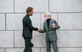 ombrello e tazza di bere. giovane tipo con anziano uomo nel elegante Abiti è all'aperto insieme. concezione di attività commerciale foto