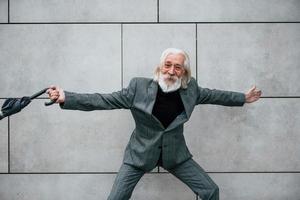 detiene ombrello. anziano uomo d'affari nel formale Abiti, con grigio capelli e barba è all'aperto foto