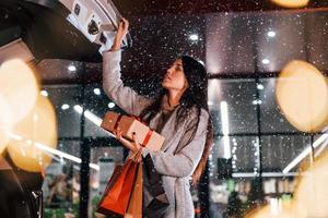 vicino il auto con regalo scatola. allegro donna è all'aperto a Natale vacanze volta. concezione di nuovo anno foto