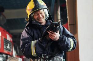 ritratto di pompiere nel protettivo uniforme quello detiene carino poco nero gatto foto