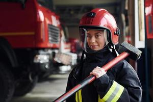 con martello nel mani. femmina pompiere nel protettivo uniforme in piedi vicino camion foto