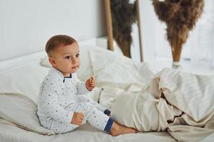 carino poco ragazzo si siede su il letto. interno e design di bellissimo moderno Camera da letto a giorno foto