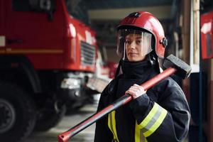 con martello nel mani. femmina pompiere nel protettivo uniforme in piedi vicino camion foto
