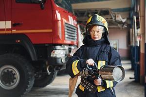 tubo flessibile nel mani. femmina pompiere nel protettivo uniforme in piedi vicino camion foto